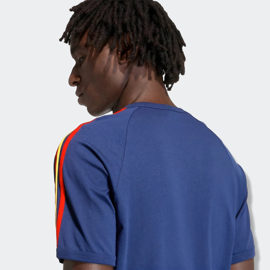 Dark-skinned man with dreadlocks wearing a blue 3-Stripes T-Shirt with red and yellow stripes, back view.