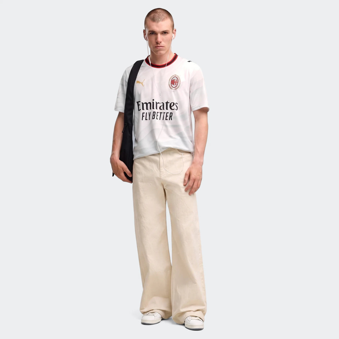 Men's AC Milan 26/27 away jersey in white, worn by a model paired with beige wide-leg pants and a black shoulder bag.
