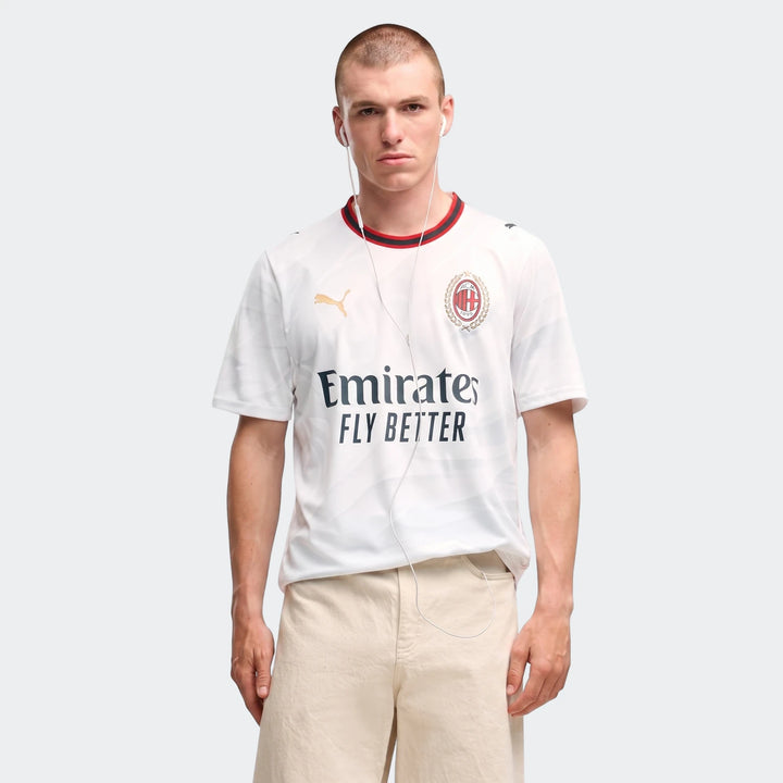 A man wears a white Ac Milan 26/27 Away Jersey, featuring sponsor logos and club crest, with short sleeves.