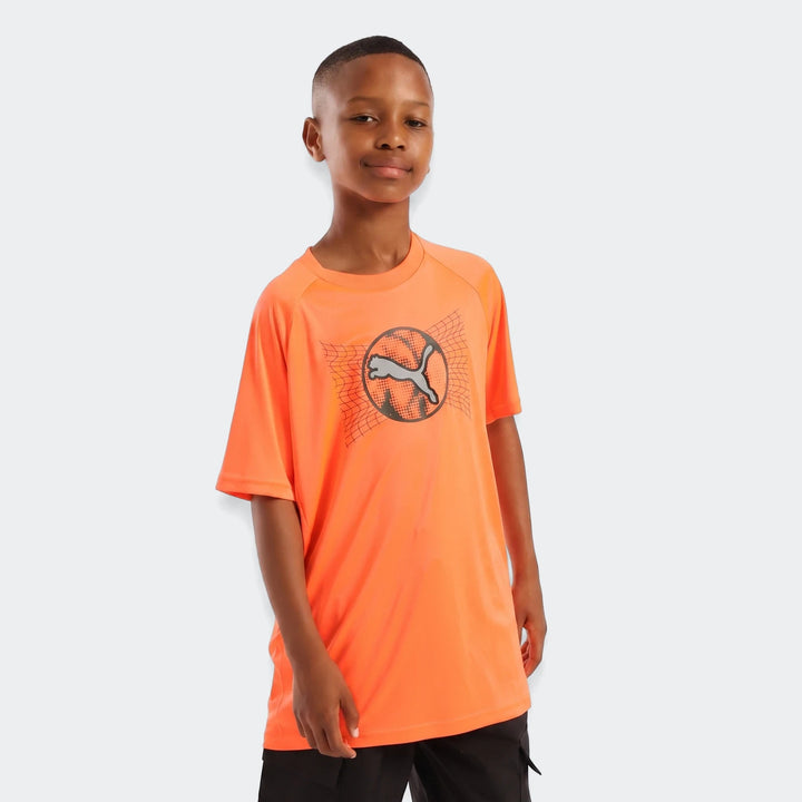 A young boy wearing an orange Puma active sports graphic t-shirt with a grey logo on the front, standing in a studio.