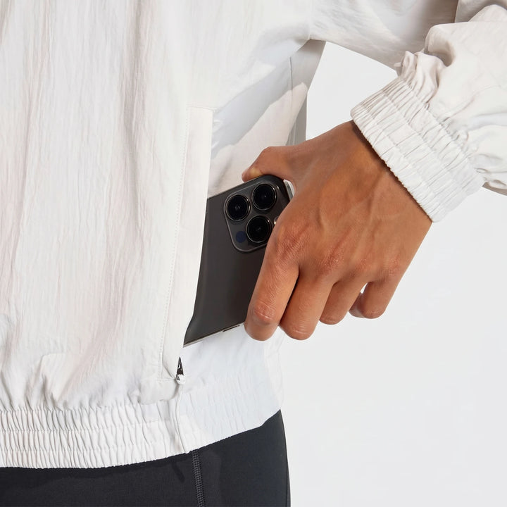 Close-up of a person's hand putting a smartphone into the pocket of an Adi365 Casual Jacket in light off-white with crinkled