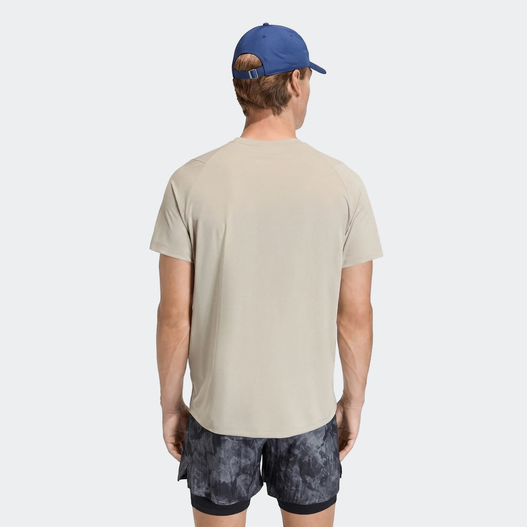 Male model from behind wearing a beige Adi365 T-Shirt, dark patterned shorts, and a blue baseball cap.