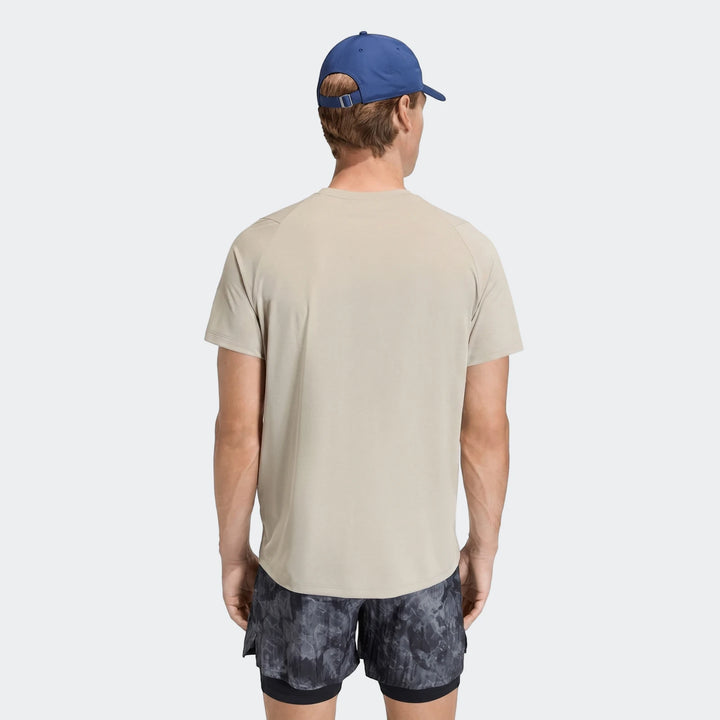 Male model from behind wearing a beige Adi365 T-Shirt, dark patterned shorts, and a blue baseball cap.