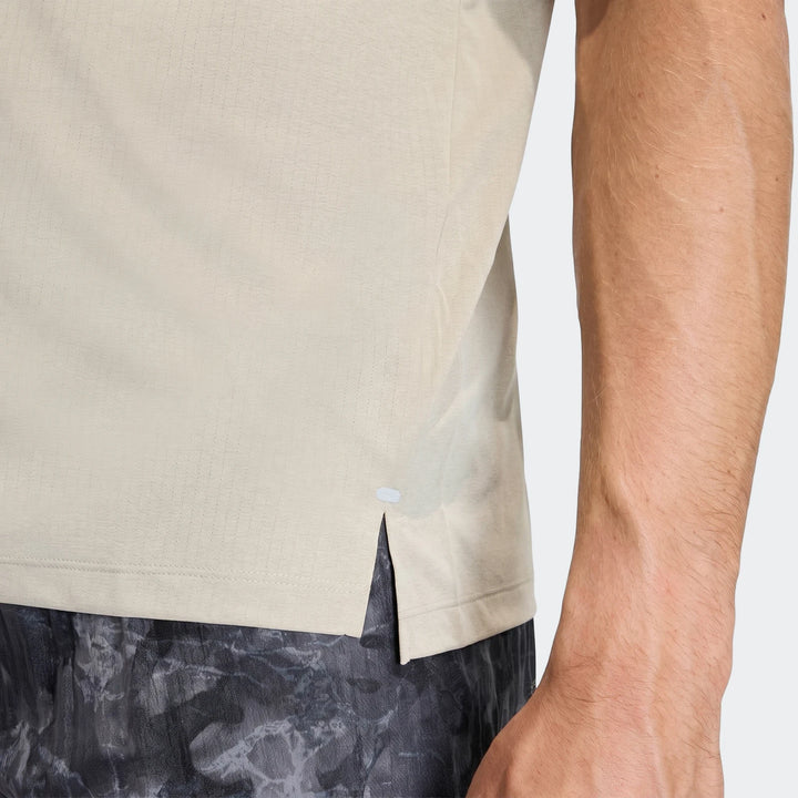 Close-up of a man wearing a light beige Adi365 T-Shirt with subtle textured fabric and dark patterned shorts.