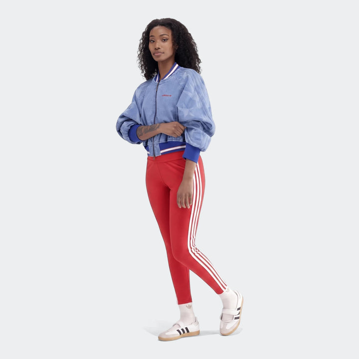 Woman wearing red Adidas 3-Stripes Cotton Leggings, blue denim bomber jacket, and white sneakers, full body view.