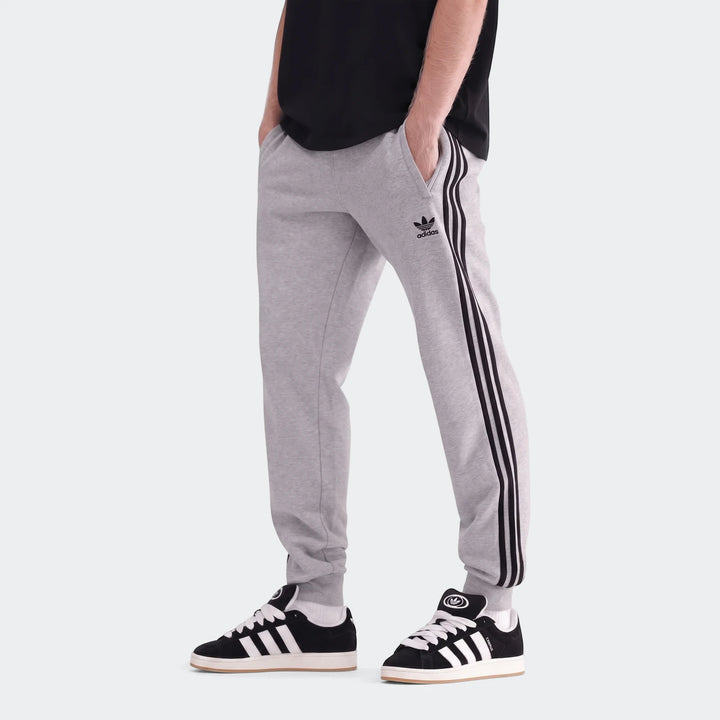 Model wears grey Adidas 3-Stripes sweatpants with black stripes, paired with black Adidas Campus sneakers and white socks.