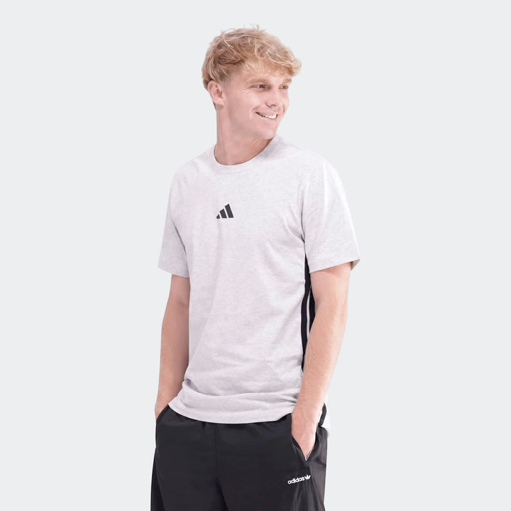 Male model wearing a light grey Adidas 3-Stripes Single Jersey T-Shirt and black shorts, looking right.