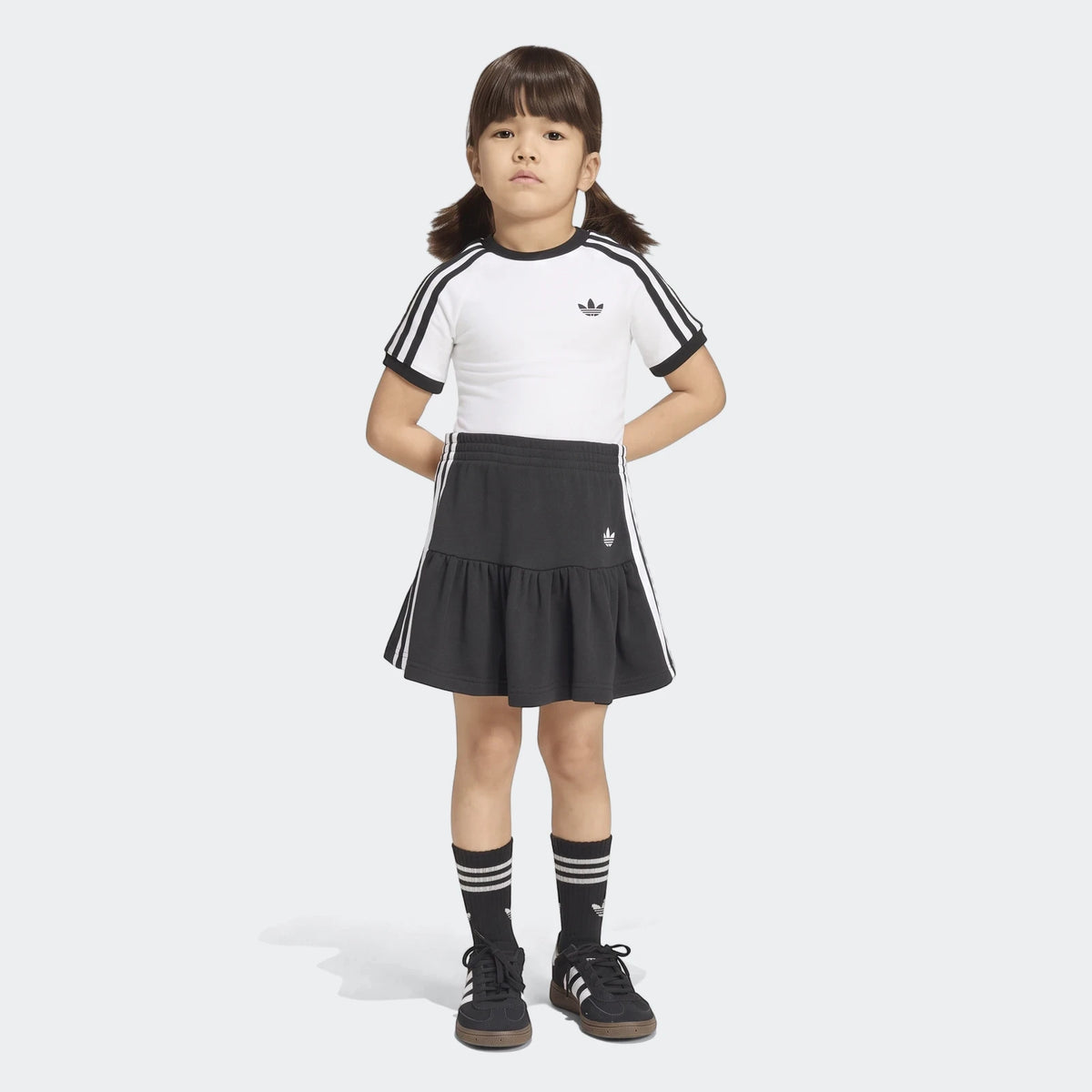 Young girl wearing an Adidas 3-Stripes Skirt Short Tee Set in black and white, featuring a white t-shirt and tiered black