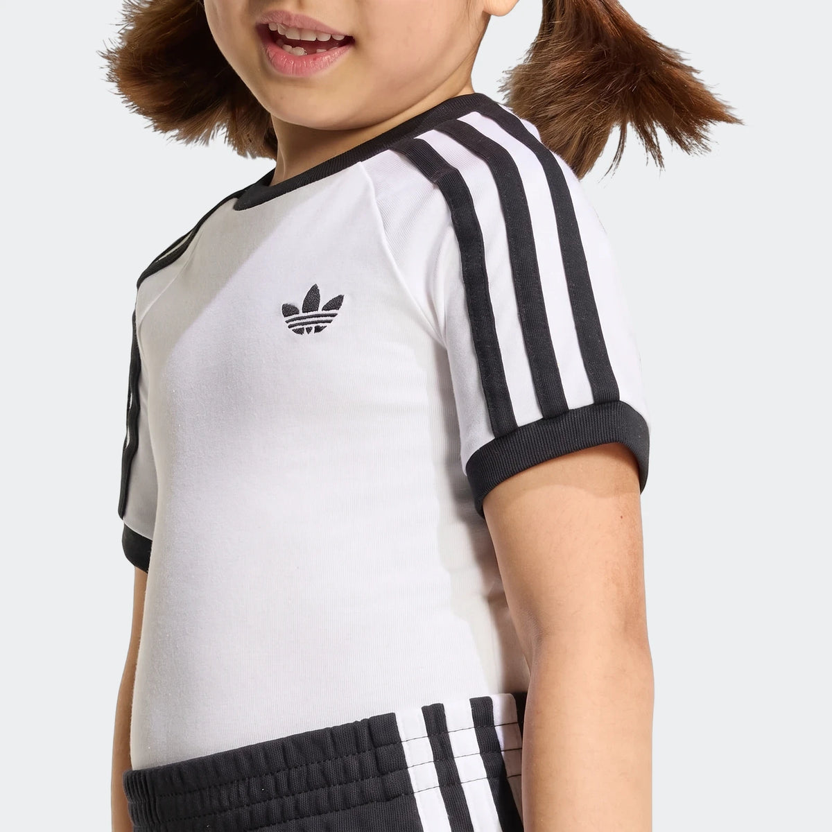 A child wears a white adidas 3-Stripes short tee with black stripes and matching black shorts for an athletic look.