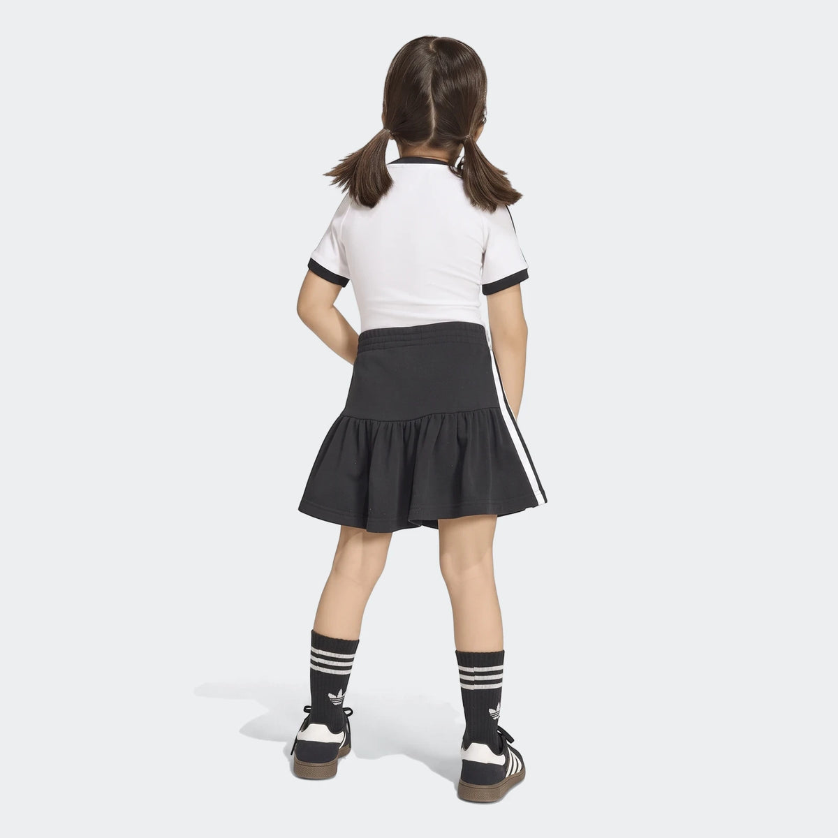 Young girl wearing a black and white Adidas 3-Stripes Skirt Short Tee Set from the back, featuring a white t-shirt and black