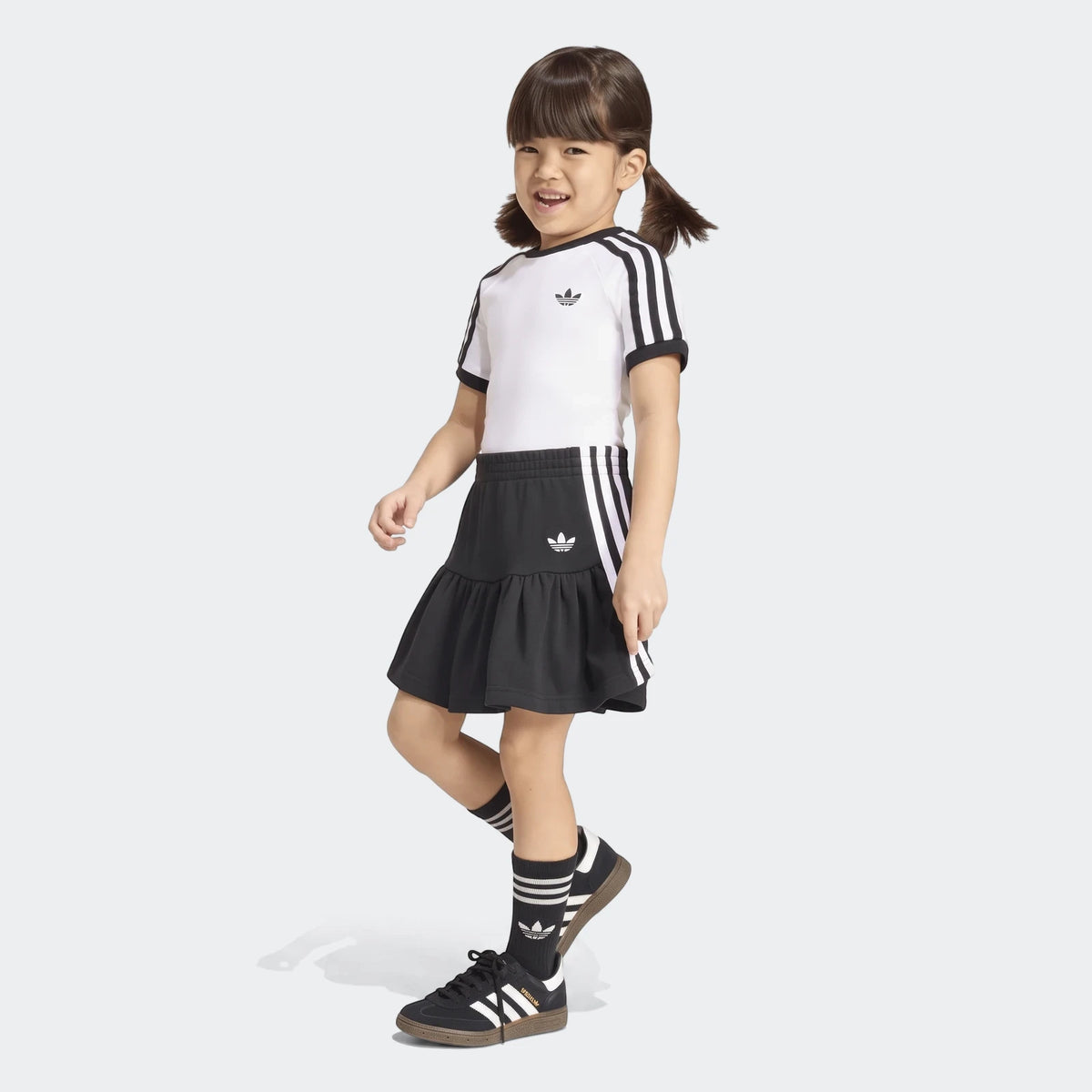 Young girl wears black and white Adidas 3-Stripes Skirt Short Tee Set, complete with matching socks and sneakers.