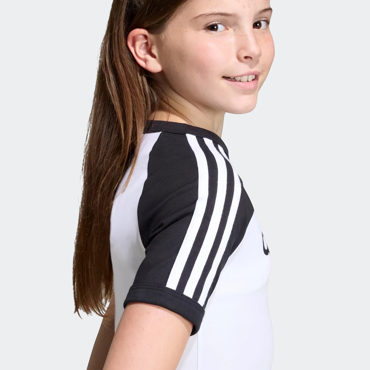 Adidas 3 Stripes Slim T-Shirt in white and black, featuring three stripes on the sleeves, worn by a young girl.