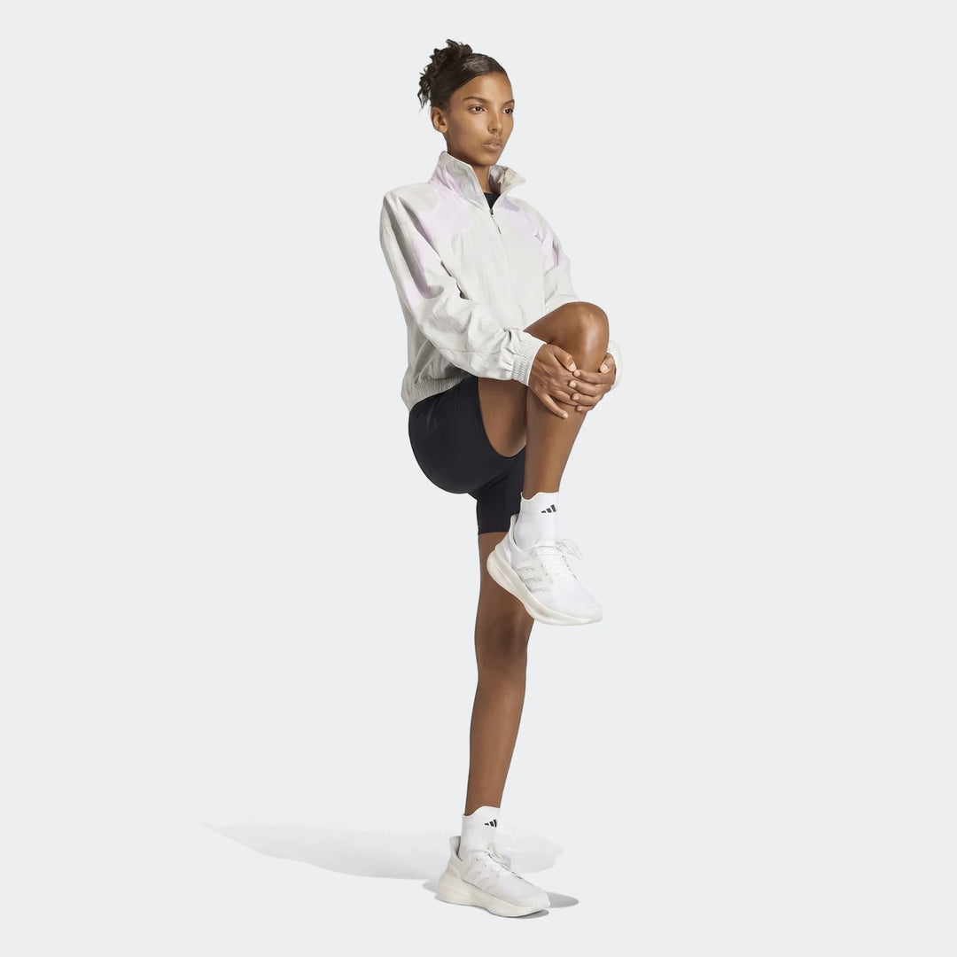 Female model wearing a light grey Adidas Adi365 Casual Jacket with pale purple panels, black shorts, and white sneakers,