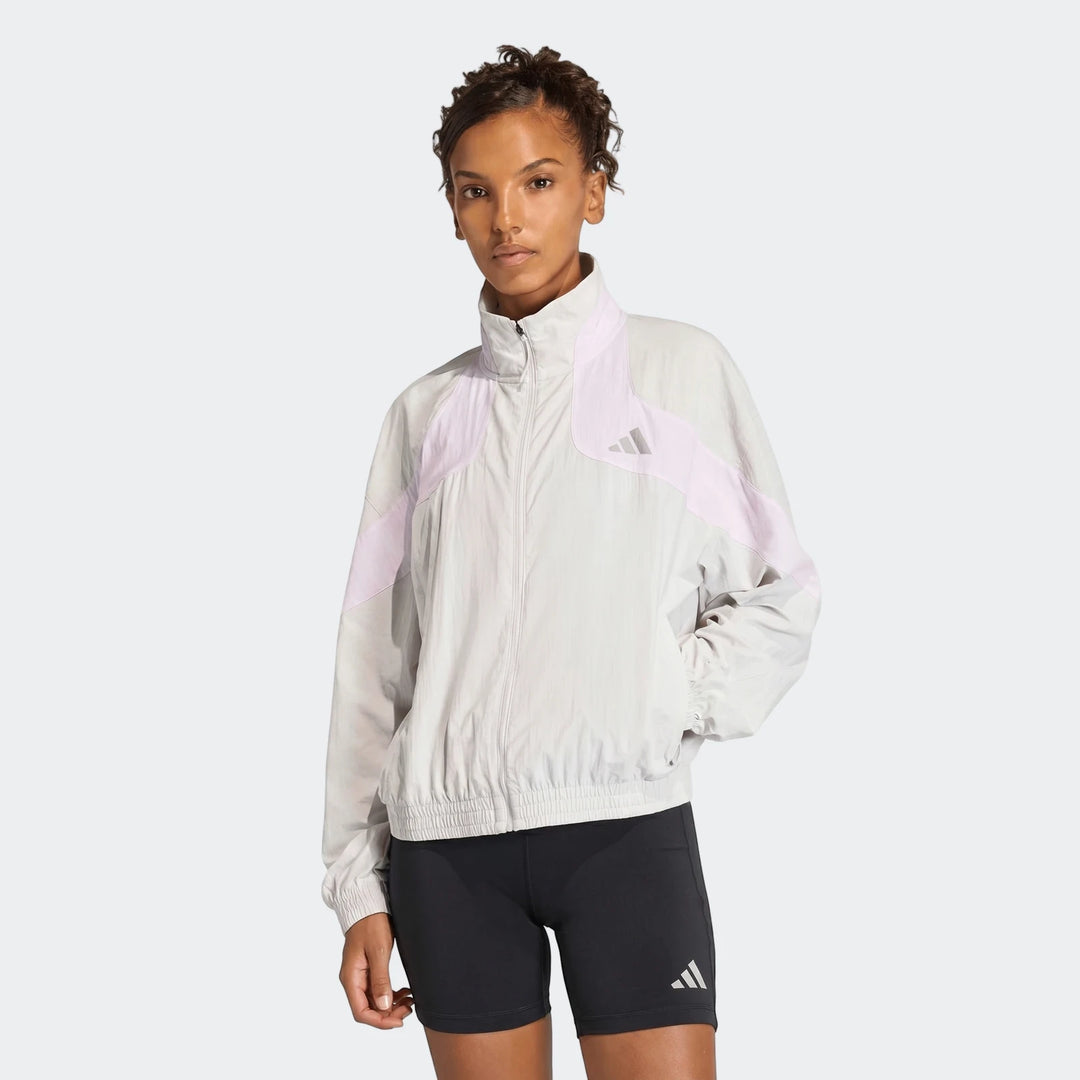 Woman wearing a light grey and pink Adidas Adi365 Casual Jacket with black cycling shorts in a studio setting.