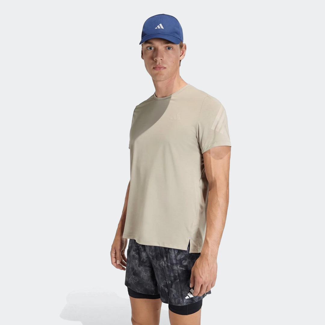 Male model poses in a light tan Adidas Adi365 T-shirt, blue Adidas cap, and black patterned athletic shorts.