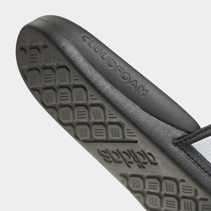 Close-up of black Adidas Adilette Comfort 2.0 slides sole, showing CLOUDFOAM and adidas branding, with textured outsole.