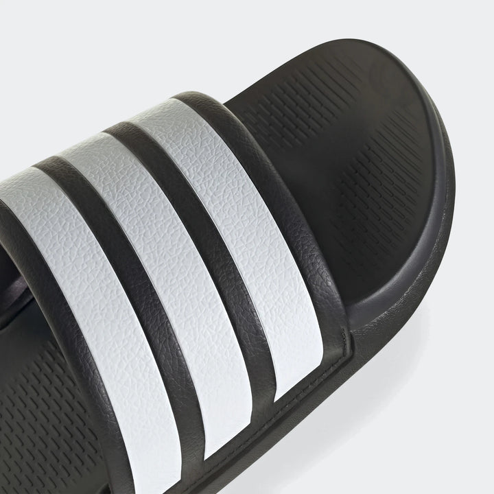 Close-up of a black Adidas Adilette slide sandal featuring three iconic white stripes on the strap and a textured footbed.