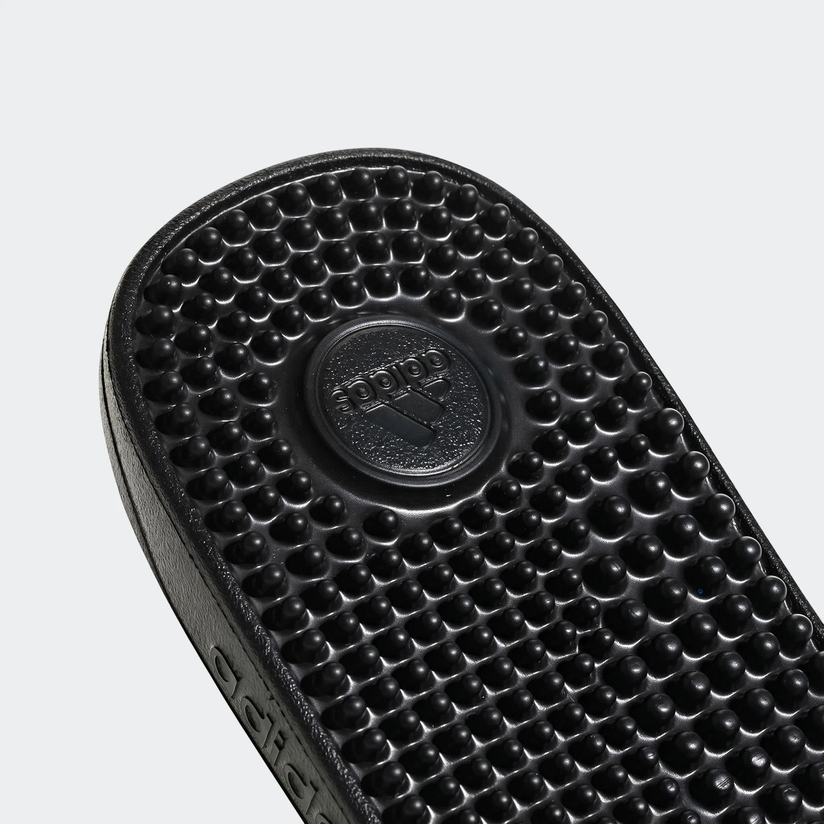 Close-up of a black Adidas Adissage slide sandal footbed, featuring a textured surface with massage nubs and embossed logo.