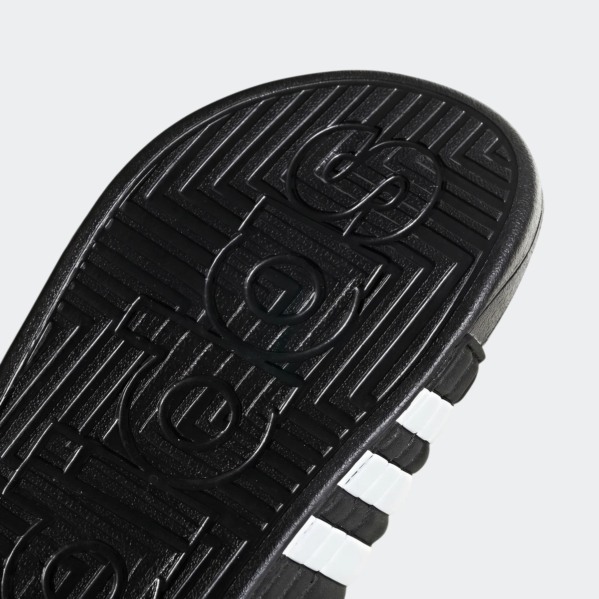 Close-up of a black Adidas Adissage slide sole, showing embossed branding and white stripes on the side.