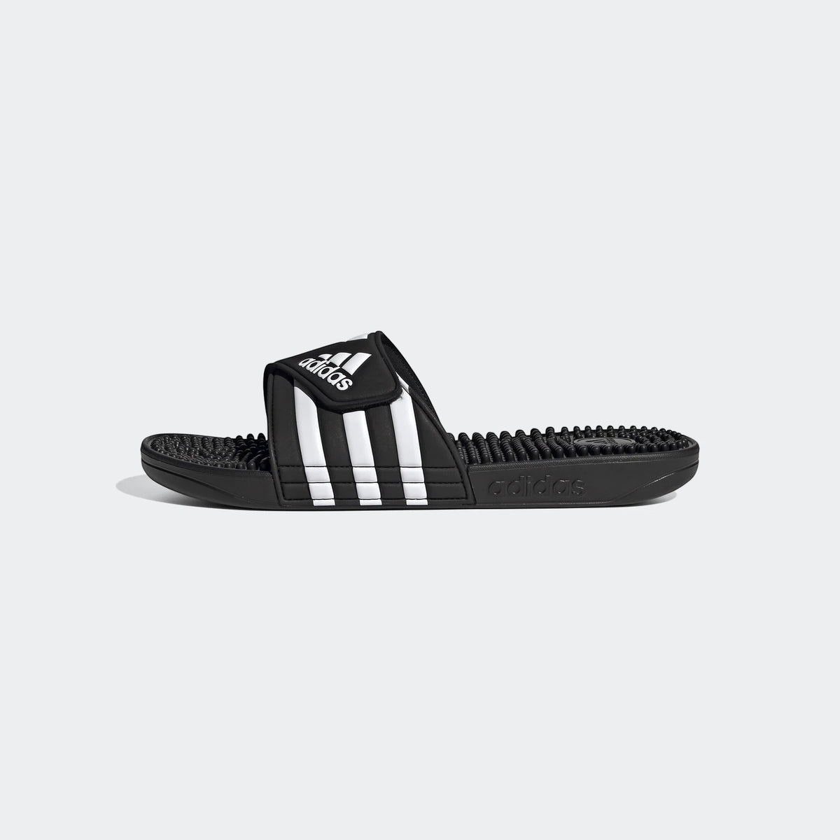 Black and white Adidas Adissage slides with three white stripes and massage footbed, shown in a side profile.