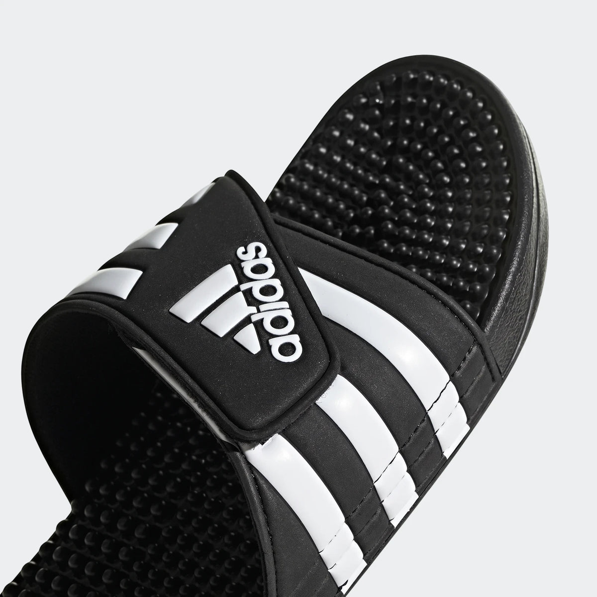 Close-up of a black Adidas Adissage slide with white stripes and the Adidas logo on the strap, showing the textured footbed.