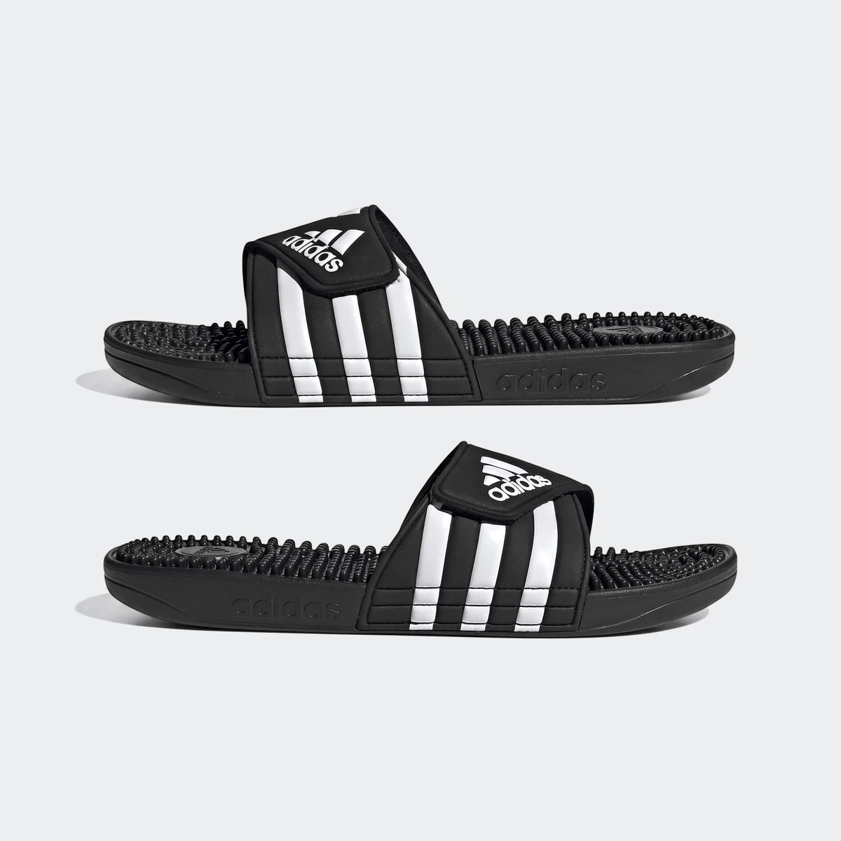 Pair of black Adidas Adissage slides with white three-stripes on the strap and a textured footbed, presented side-by-side.