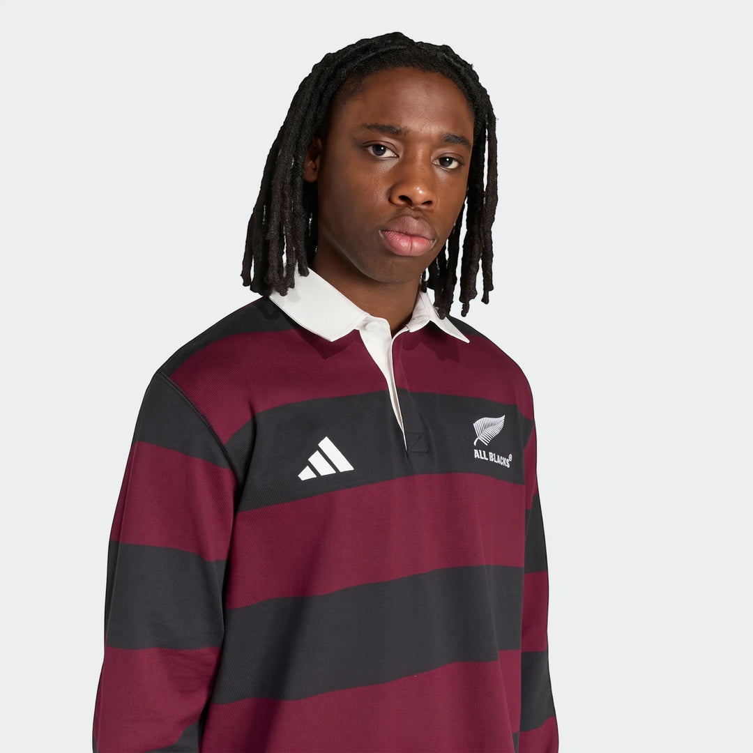 Young male model wearing an Adidas All Blacks Heritage Polo shirt featuring black and maroon horizontal stripes.