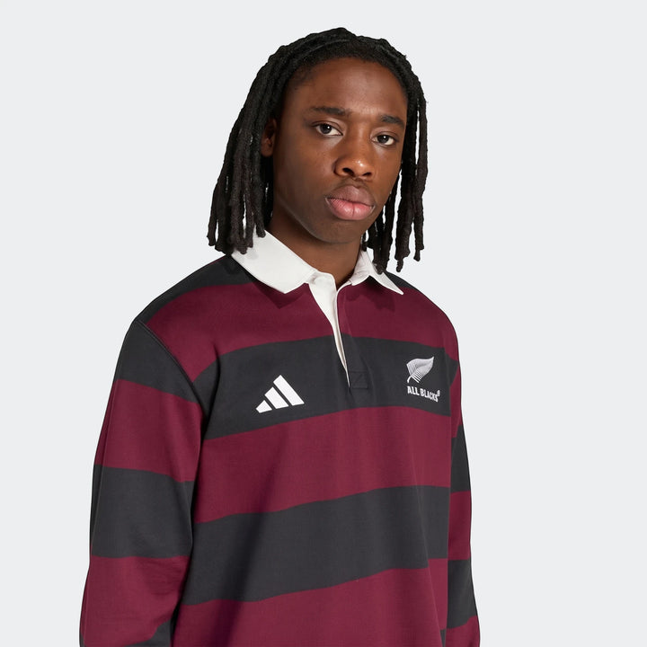Young male model wearing an Adidas All Blacks Heritage Polo shirt featuring black and maroon horizontal stripes.