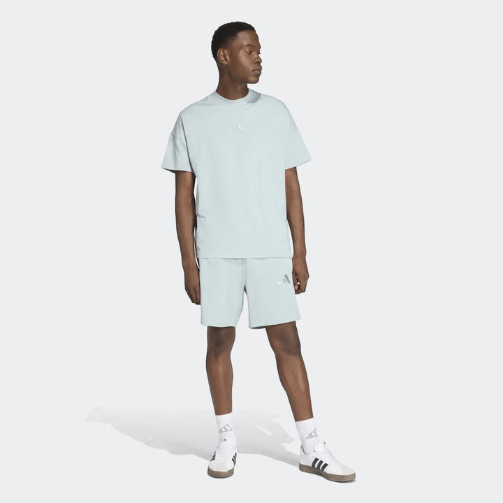 Male model wearing an Adidas All Season T-shirt and matching shorts in light green with white sneakers, posed in a studio.