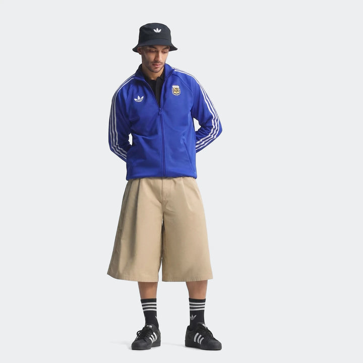 Male model wearing a blue Adidas Argentina Originals Track Top, paired with khaki culotte shorts, black socks, and a black