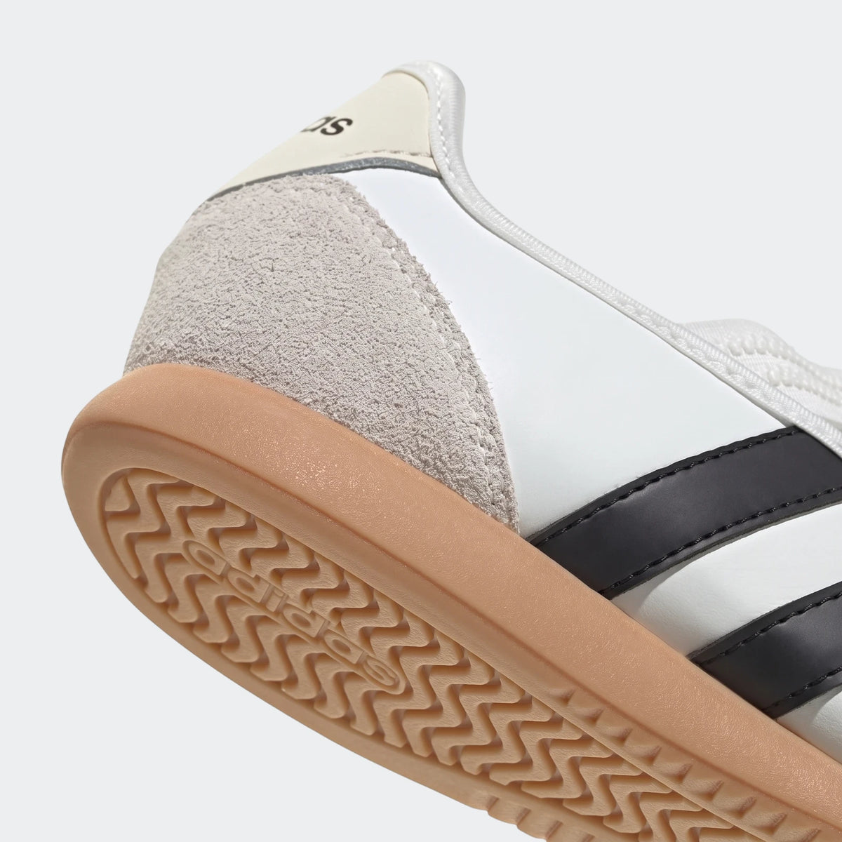 Close-up of a white Adidas Barreda Mary Jane shoe with black stripes, light grey suede details, and a tan gum sole.