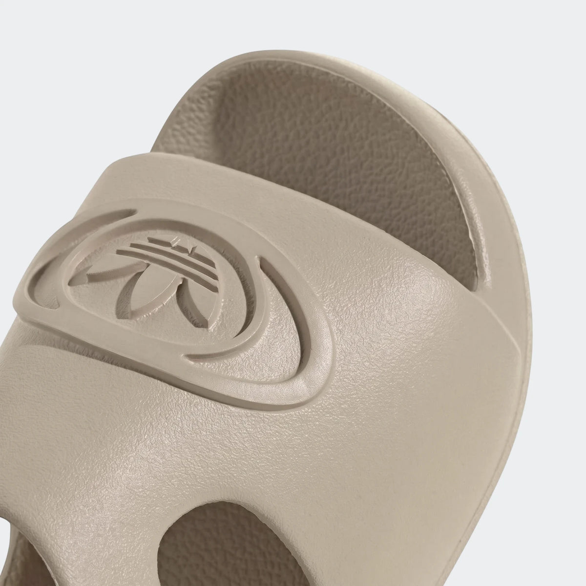 Close-up of a light beige Adidas Campus 00S Foam Slide, showing the textured strap and embossed Trefoil logo on a white