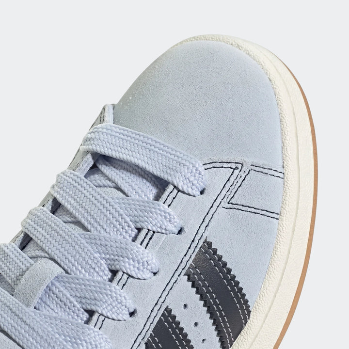 Close-up of Adidas Campus 00S shoes in light blue suede, featuring iconic dark gray three stripes and an off-white sole.