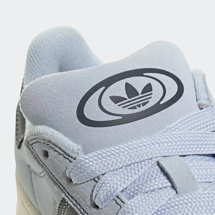 Close-up of the light blue suede Adidas Campus 00S shoe, highlighting the tongue with the dark Trefoil logo and textured