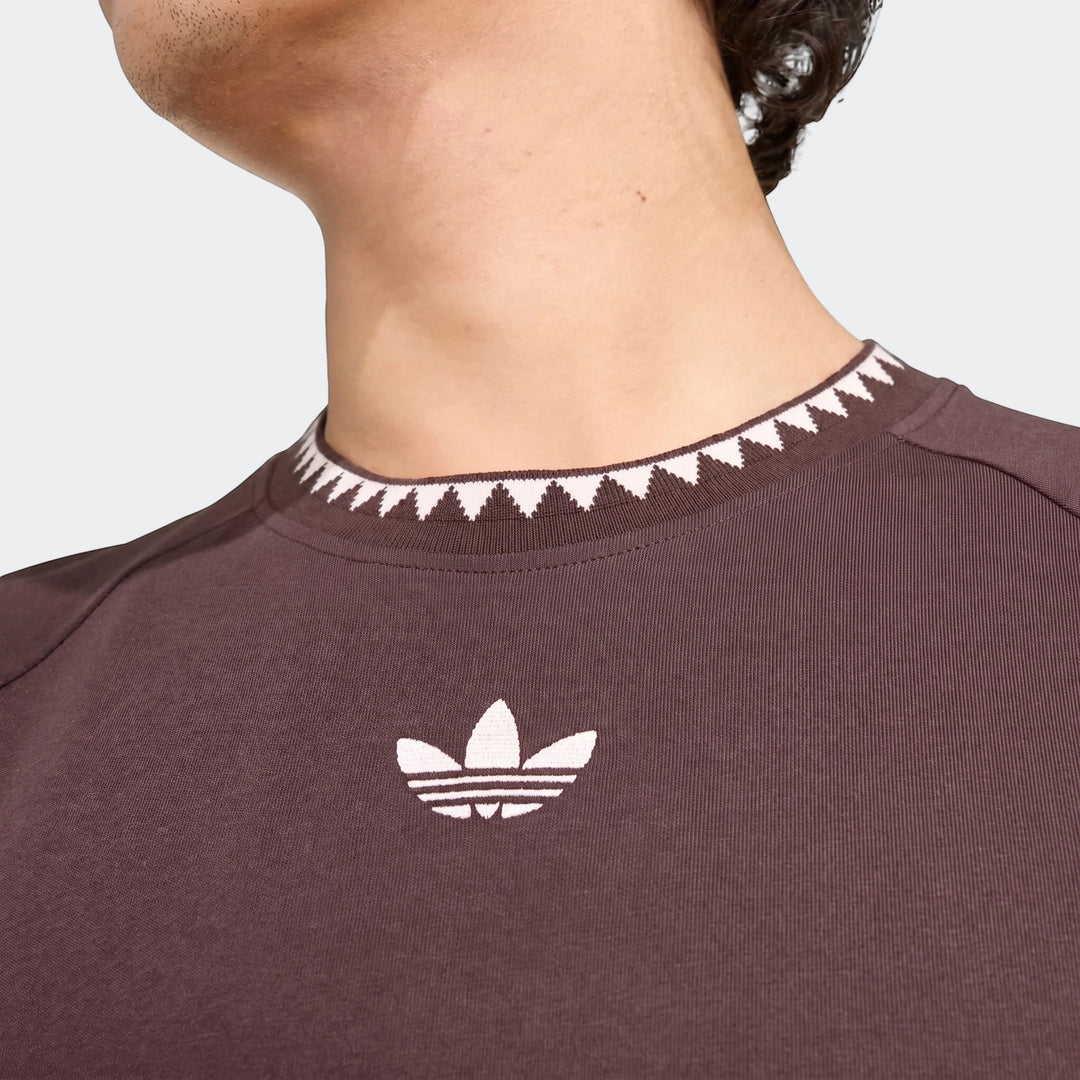 Close-up of a person wearing a brown Adidas Chest Stripe Short Sleeve T-Shirt with white triangular collar pattern.
