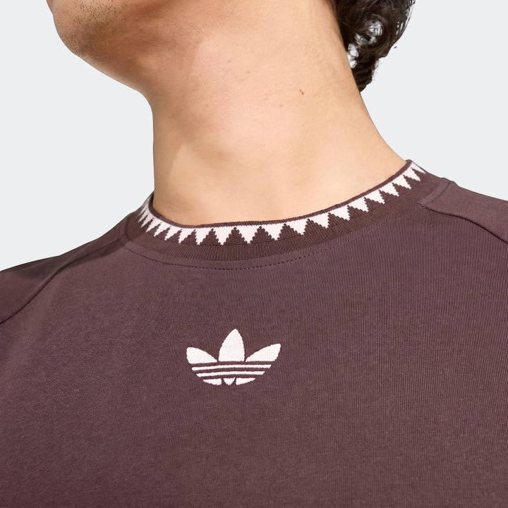 Close-up of a person wearing a brown Adidas Chest Stripe Short Sleeve T-Shirt with white triangular collar pattern.