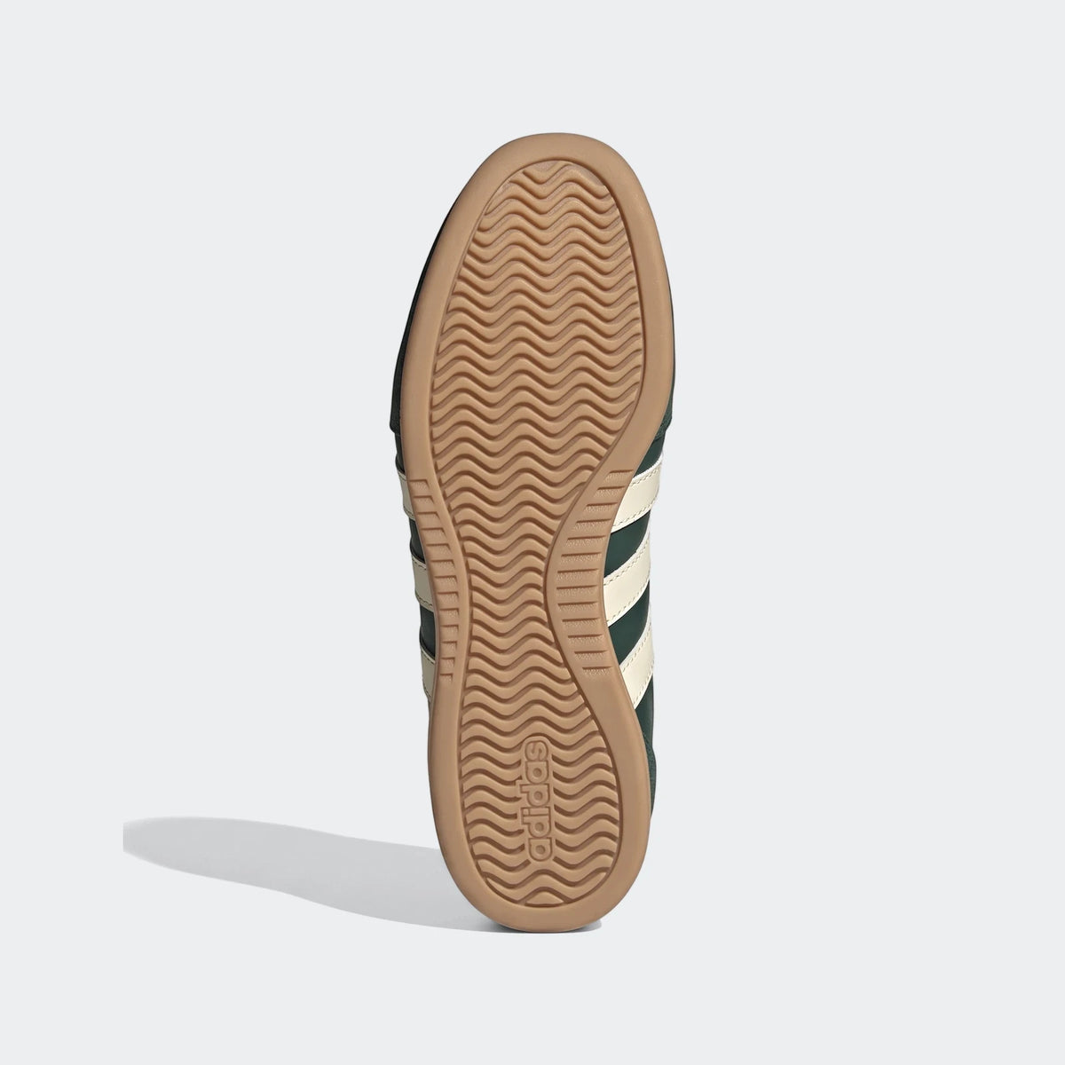 Bottom view of a dark green Adidas sneaker with cream stripes, featuring a light brown gum rubber sole with wavy traction