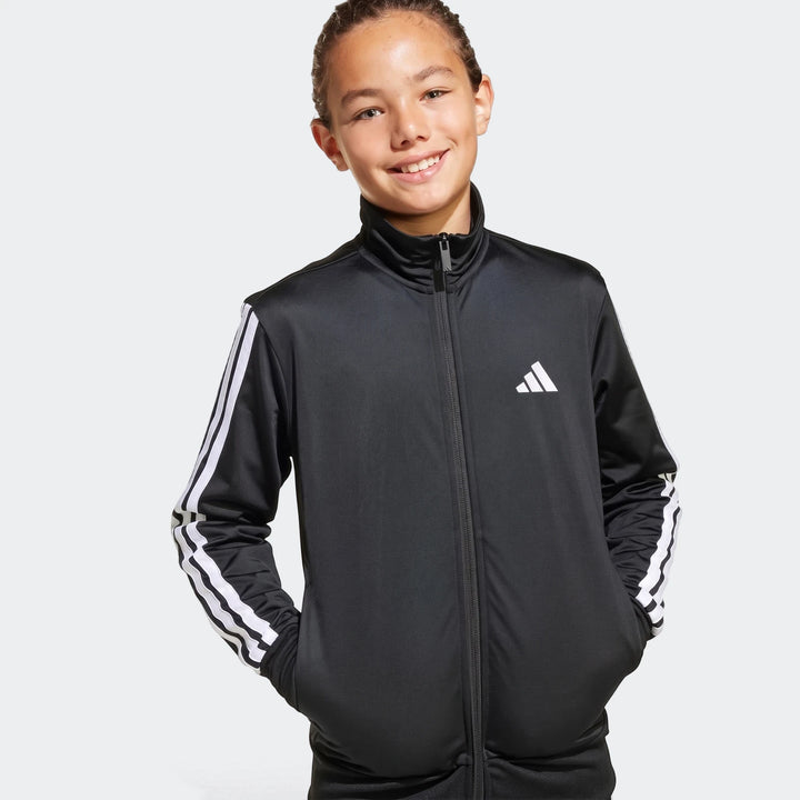 Smiling young person wearing a black Adidas Essentials Climacool track jacket with white three stripes on the sleeves.