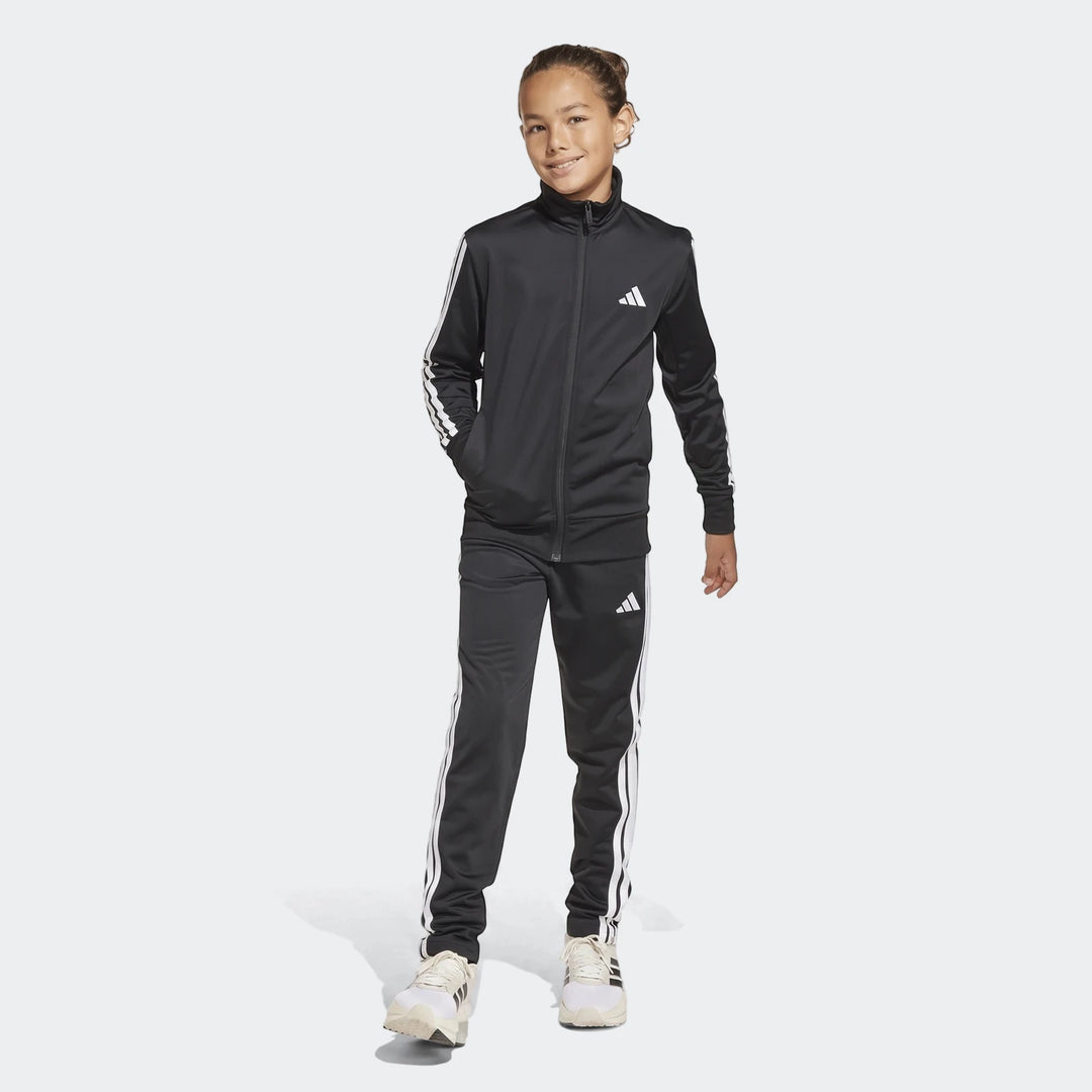 Black Adidas Essentials Climacool Track Suit for kids, featuring white 3-stripes, shown full-body on a smiling young model.