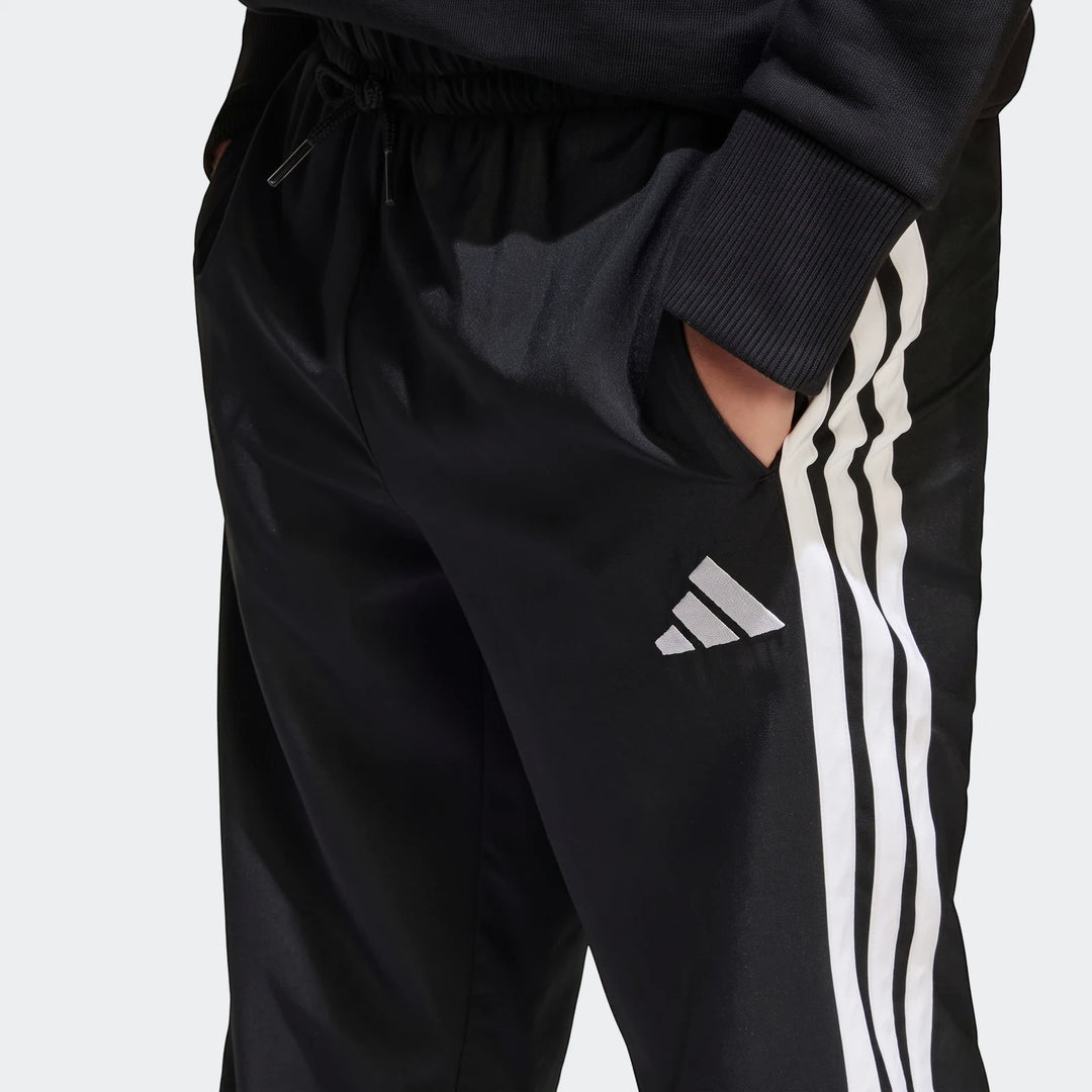 Close-up of black Adidas Essentials Climacool kids' tracksuit bottoms with white stripes and logo, worn by a person.
