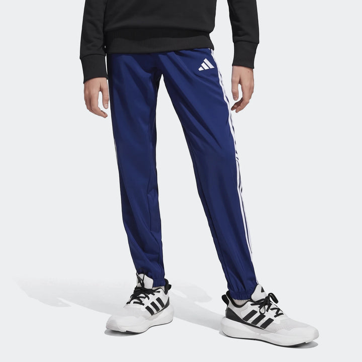 Kid's Adidas Essentials Climacool tracksuit bottoms in royal blue with white stripes and logo, worn with white sneakers.