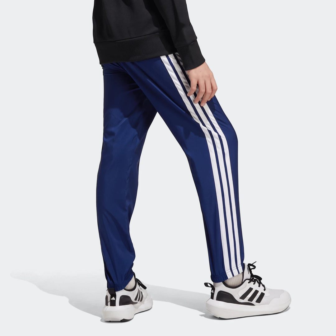Kids' Adidas Essentials Climacool tracksuit bottoms in royal blue with classic white stripes, worn with white sneakers.