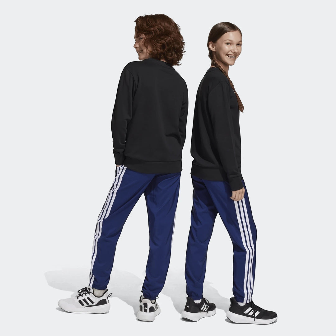 Two children wearing black sweatshirts and blue Adidas Essentials Climacool Tracksuit Bottoms with white stripes and