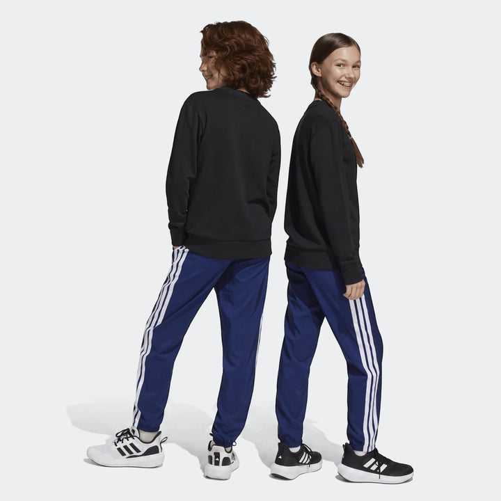 Two children wearing black sweatshirts and blue Adidas Essentials Climacool Tracksuit Bottoms with white stripes and