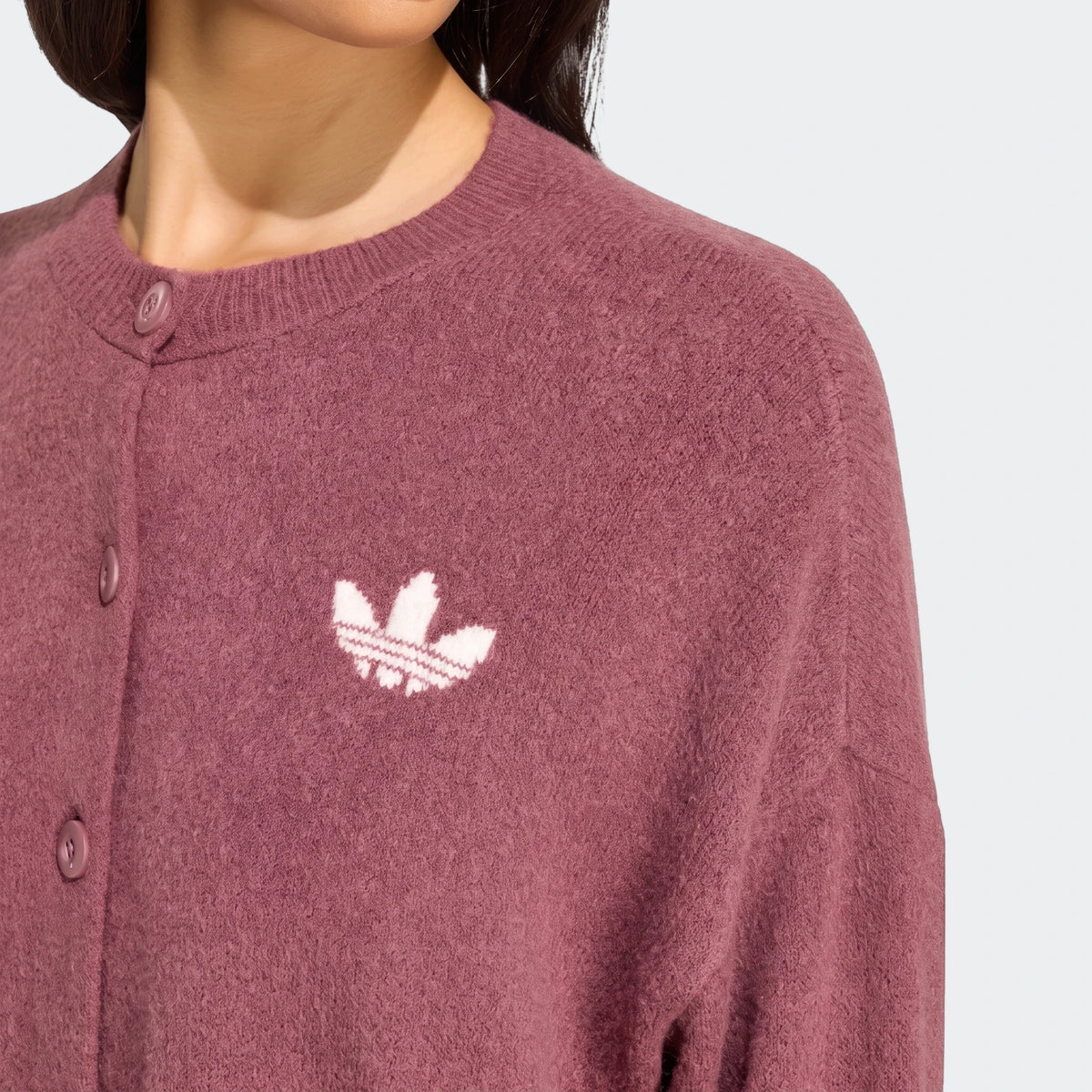 Close-up view of a dusty pink Adidas Essentials knit cardigan worn by a model, featuring a white Trefoil logo and front