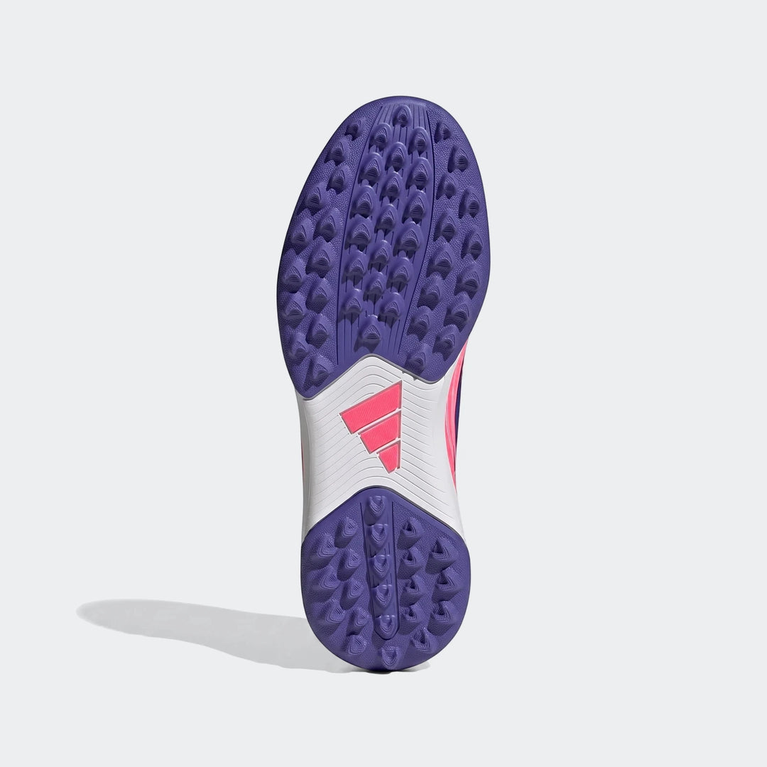 Bottom view of kids' Adidas F50 Hyperfast Club turf football boots in purple, pink, and white, featuring a studded outsole