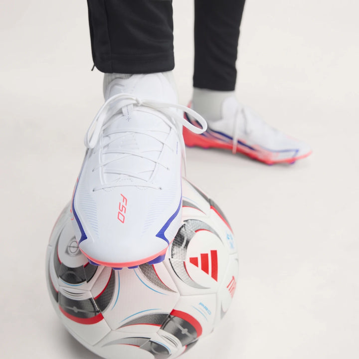 White Adidas F50 Hyperfast League Firm Ground Football Boots worn by a person, with one foot resting on an Adidas football.