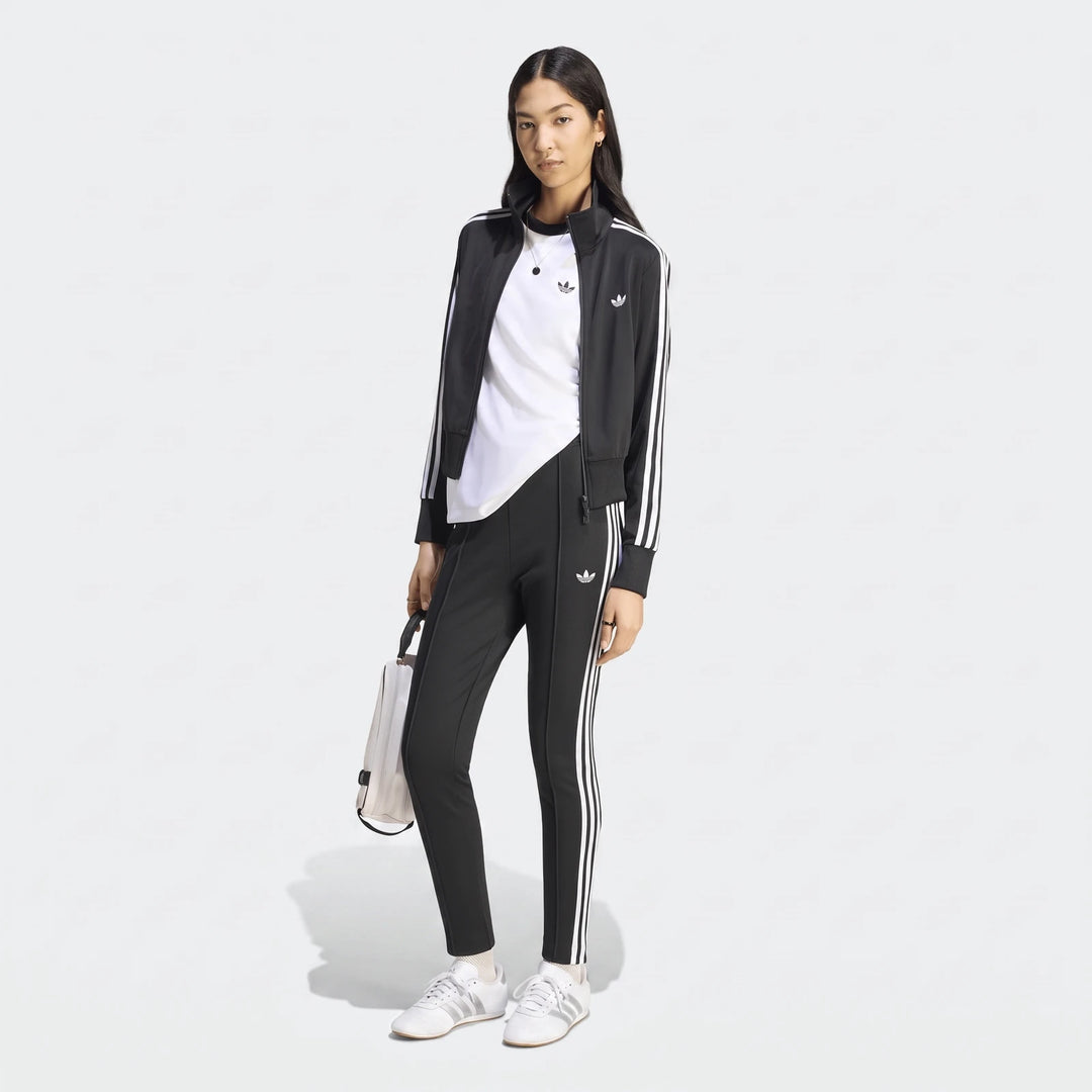 Female model in a black Adidas Firebird Classic Track Jacket with white stripes, matching track pants, white t-shirt, and