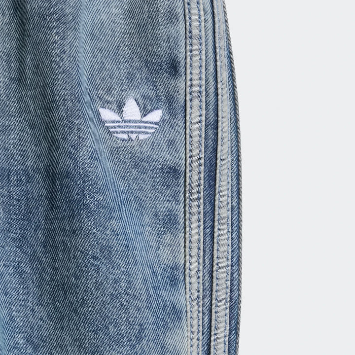 Close-up of blue Adidas Firebird denim track pants, showing the embroidered white Trefoil logo and light blue side stripes.