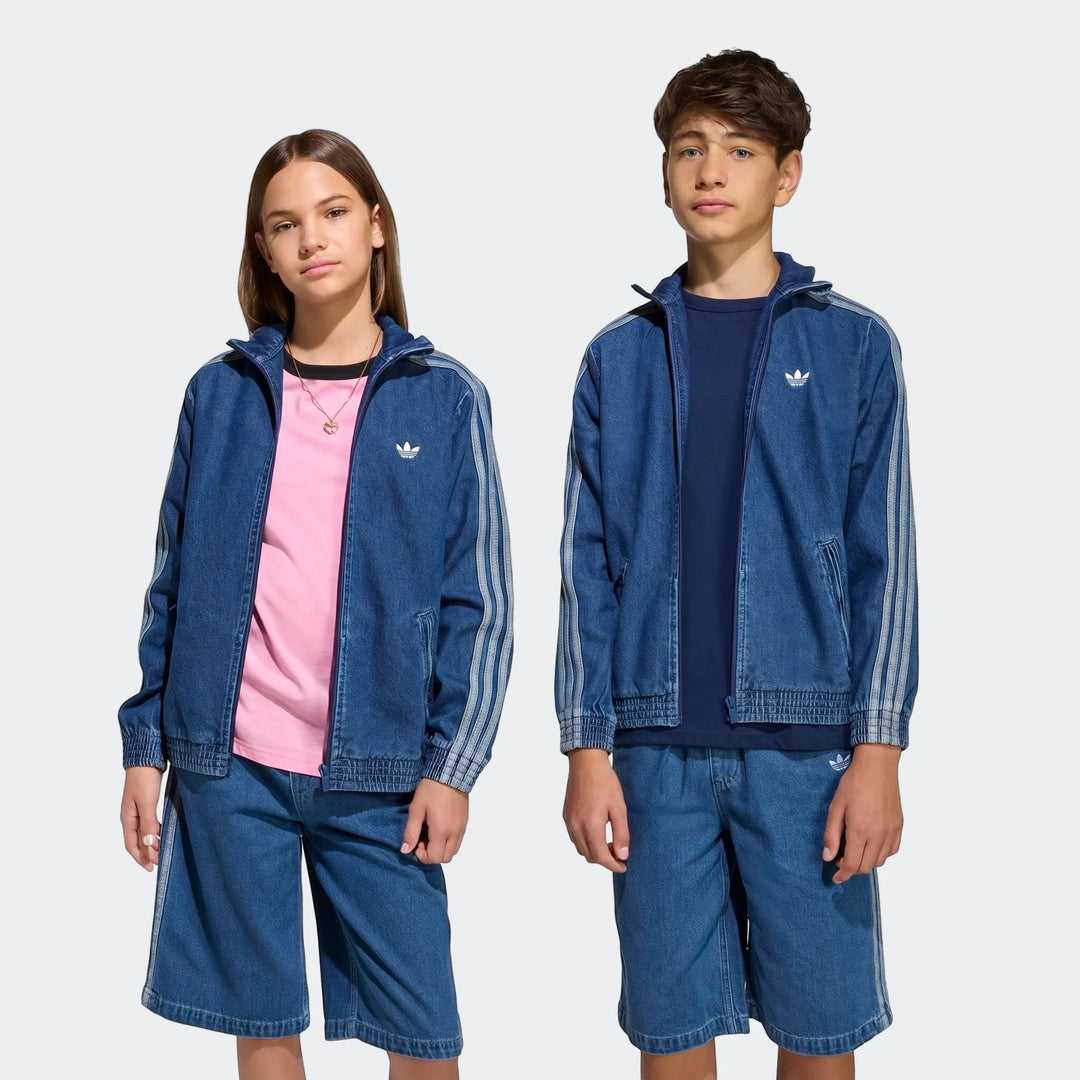 Two young models, a girl and a boy, wearing matching blue Adidas Firebird Denim Track Tops and coordinating shorts,